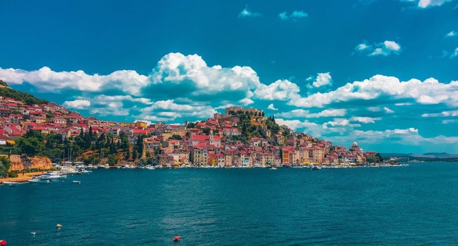 Pogled na Šibenik uz more, središnji dio grada i šarenim kućama pod plavim nebom s oblacima